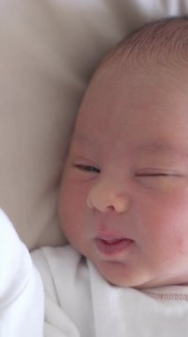 Işık bezi içinde küçük şirin bir bebeğin yakın görüntüsü. Beyaz battaniyeye uzanmış güzel bir bebek. Dikey video