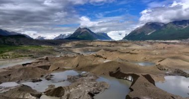 Ice melts in the valley of Alaska, USA. Fluffy clouds cover the tops of the mountains at backdrop.