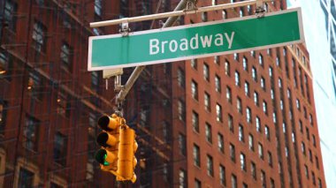 New York 'ta trafik ışığı olan bir Broadway tabelası. Trafik lambası yeşil parlayan bir Broadway sokak tabelası. Arka planda Manhattan, New York 'ta kırmızı tuğlalı bir bina yer alıyor..