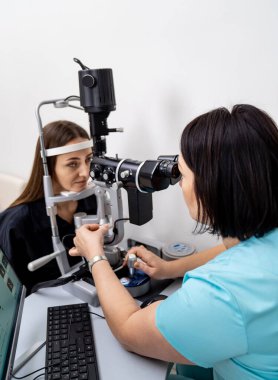 Hasta yarık lamba göz muayenesinden geçiyor. Doktor tarafından işletilen oftalmik tanı cihazına bakan genç bir kadın..