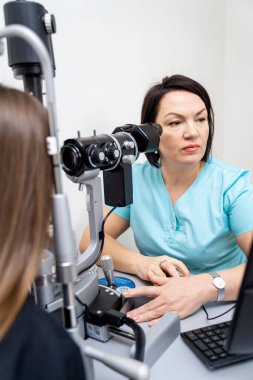 Görme testi sırasında oftalmolog hastaya danışıyor. Klinikte uzman. Göz muayenesi için kesik lamba kullanıyor..