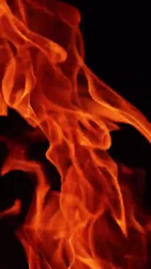 Karanlıkta hareket eden turuncu ateş dilleri. Siyah arka planda izole bir şekilde yanan şenlik ateşinin yakın görüntüsü. Dikey video