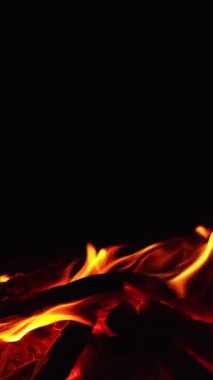 Kamp ateşinde odun yakmak. Sola doğru hareket eden küçük alevlerle şenlik ateşi yakıyor. Kapatın. Siyah zemin. Dikey video