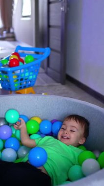 Joyful energetic Caucasian toddler tumbling in the dry pool. Little kid getting out of the basin. Vertical video