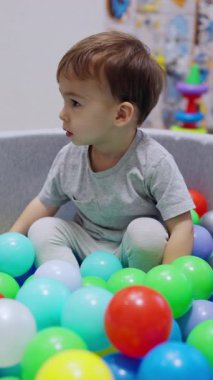 Sakin bebek kuru havuzda hayaların içinde oturur. Bebek topların üzerine yatar ve havuzda rahatlar. Dikey video