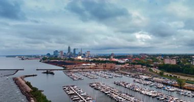 Numerous boats stand at the berths in the yacht club of Cleveland, Ohio, USA. City panorama under the grey overcast sky from drone footage.