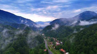 Romanya 'da bulutlu dağ vadisi. Romanya 'nın Karpatlar bölgesindeki manzaralı bir dağ vadisi ve köyün üzerinde puslu bulutlar asılı..