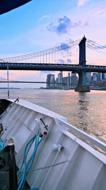 On board of the boat travelling by the East River. Low angle view at the Manhattan Bridge and New York skyline at sunset time. Vertical video.