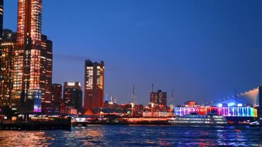 Fantastic illumination of the buildings and streets at the waterfront of the East River. Diverse boats arrive to the pier at dusk time.