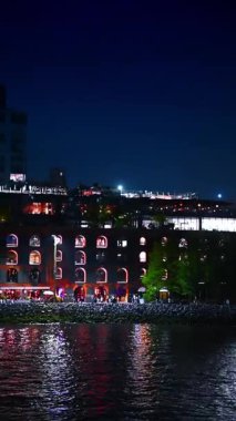 Watching a beautifully illuminated buildings at the waterfront of the city at night. Boat tour around New York, USA. Vertical video.