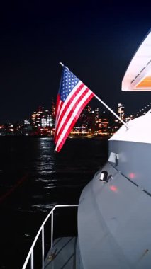 Standing on board of the boat with an American flag. Night river tour around the modern city. Vertical video.