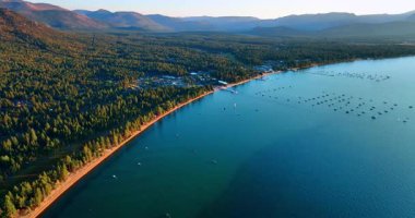 Lake Tahoe waterscape with wooded lakefront. Drone footage at the shore. Multiple boats stand on the water.