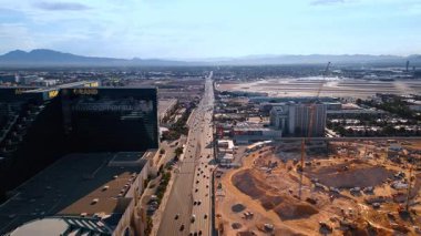 Las Vegas, USA, 11 September 2025: Flight above the multi-lane highway with multiple cars moving by near the construction site. Turning to the dark buildings of the MGM Grand Garden Arena in Las Vegas, Nevada, USA. Aerial view.