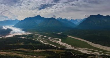 Vast nature landscape of spectacular Alaska, USA. Drone footage over the valley with rivers surrounded by the mountains. Fluffy clouds covering the sky over the scenery.