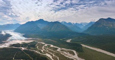 Uneven valley with a branching river. Spectacular mountains of Alaska, USA at backdrop. Sky covered by stratus clouds.