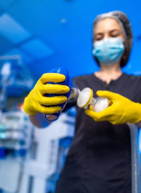 Hemşire havalandırma maskesi hazırlıyor. Hastane ameliyathanesinde siyah üniformalı ve sarı eldivenli, havalandırma maskesini hazırlayan sağlık hemşiresine yakın çekim..