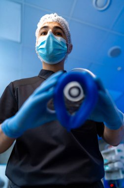 Anestezi maskeli bir cerrah. Koruyucu maskeli doktor ameliyathanede anestezi ekipmanı tutuyor..