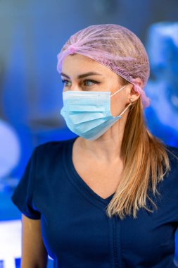 Koruyucu maskeli kadın doktor. Mavi önlüklü ve maskeli doktor hastanede yan bakıyor..