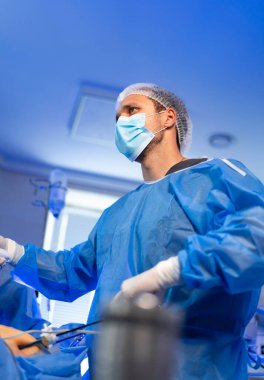 Laparoskopik enstrüman tutan bir cerrah. Tıbbi prosedür sırasında elinde laparoskopik enstrüman tutan mavi cerrahi önlüklü doktor..