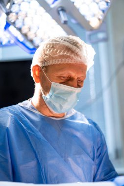 Cerrah ameliyat sırasında konsantre oluyor. Maskeli ve cüppeli doktor cerrahi işleme odaklanmış.