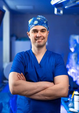 Mavi üniformalı gülümseyen bir cerrah. Çapraz kollu mavi cerrahi giysili doktor.