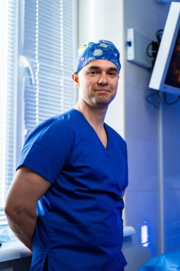 Cerrah ameliyathanede bekliyor. Tıbbi ekipmanların yanında mavi cerrahi giysili bir doktor.