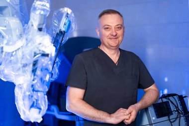 Robot cerrahi ekipmanlı bir doktor. Tıbbi uzman mavi ışıklı ameliyathanede robotik cerrahi kolların yanında duruyor..