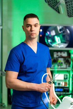 Klinikte tıbbi uzman cerrahi enstrüman inceliyor. Hastane ameliyathanesinde laparoskopik cerrahi aletlere bakan mavi önlüklü bir doktor..