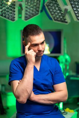 Ameliyathanede cerrah düşüncesi. Mavi önlüklü doktor. Ameliyathanede düşünceli bir yüz ifadesi var..