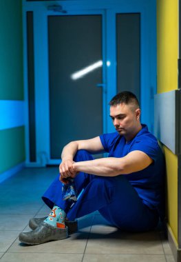 Hastane koridorunda oturan bir cerrah. Önlüklü doktor hastanede tek başına oturmuş düşünceli bir şekilde bakıyor..