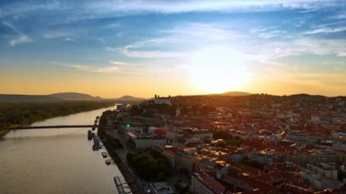 Batan güneş, Slovakya 'nın Bratislava kentinin manzarasını aydınlatıyor. İnsansız hava aracı görüntüleri Tuna suları üzerinde ve şehir manzarası gün batımında.