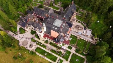 Romanya 'nın Prahova İlçesi' ndeki Peles Kalesi 'nin çatısından uçuyor. Birden fazla insan şehir simgesini ziyaret ediyor ve bölgeye doğru yürüyor..