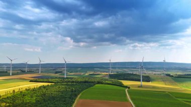 Rüzgâr tarlalarıyla vurulan yeşil yaz tarlaları. Bulutlu bir günde kırsal bölgede İHA uçuşu.