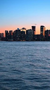 New York, ABD 'deki gökdelenlerin siluetleri. Gün batımında nehir manzarası. Dikey video.