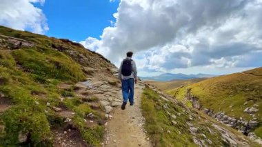 Busteny, Romania, 17 July 2025: Hiker on mountain trail in Bucegi range. Person hiking along mountain trail in Bucegi Mountains with cloudy sky.