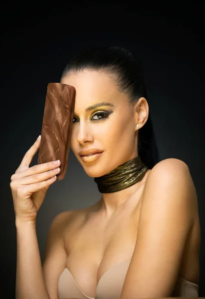漂亮性感的年轻黑发女人穿着金色化妆品吃巧克力 — 图库照片