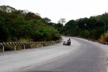 Angono, Rizal, Philippines - March 19, 2024: A man rides his tricycle in an empty provincial road. clipart