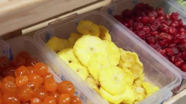 Tek kullanımlık eldiven giyen kadın mağaza çalışanı mağazadaki bir rafa kurumuş egzotik meyveler koyar. Satıcı kadın raflarda kurumuş ananas halkalarını yeniler, bir markette çalışır.. 