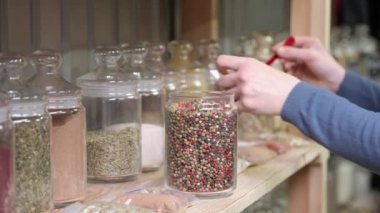 Satıcı kadın eli, satış rafının yanındaki plastik poşette kırmızı ve siyah biber karışımı bir şey koyar. Markette baharatlar, yavaş çekim.