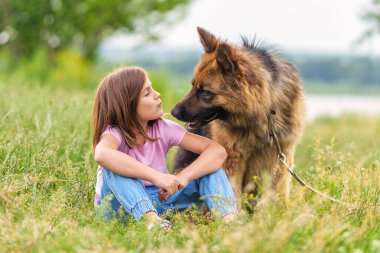 Yazın parkta çimlerde oturan çoban köpeğini öpen tatlı küçük kız. Yüksek kaliteli fotoğraf, bulanık arkaplan