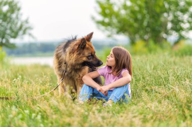 Yazın parkta çimlerde oturan çoban köpeğini öpen tatlı küçük kız. Yüksek kaliteli fotoğraf, bulanık arkaplan