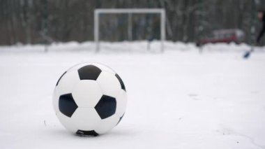 Futbol topu kalenin önünde, karla kaplı mini futbol sahasının ortasında yatarken, arkasında kimliği belirsiz bir adam kar küreğiyle tarlayı temizliyor.