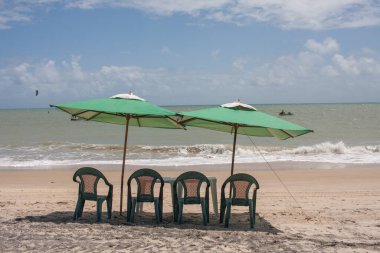 Brezilya, Combuco sahilinde küçük bir masaya kurulmuş iki yeşil şemsiye.