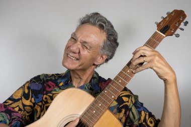 Senior man wearing a colorful shirt playing his guitar 