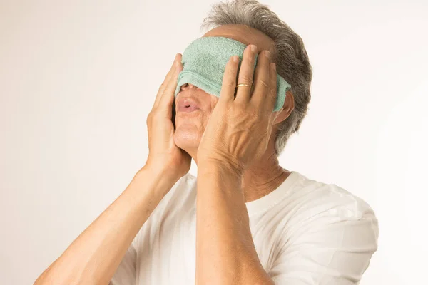 Older man with a warn compress over his eyes for pain relief