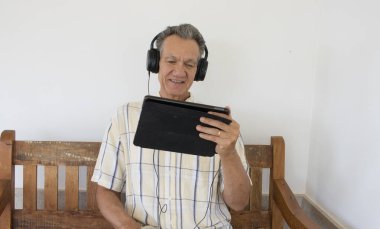 Dışarıda oturan olgun bir adam iPad Smart tabletinde kulaklık takmış bir dizi izliyor.