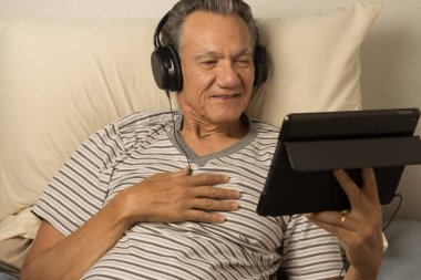 Kulaklık takmış, iPad 'inde film seyreden yetişkin bir adam.