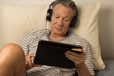 Kulaklık takmış, iPad 'inde film seyreden yetişkin bir adam.