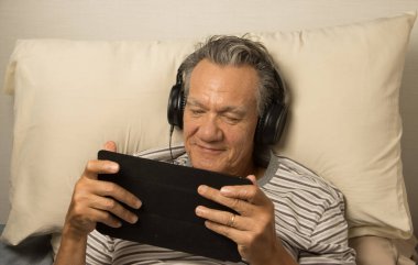 Kulaklık takmış, iPad 'inde film seyreden yetişkin bir adam.