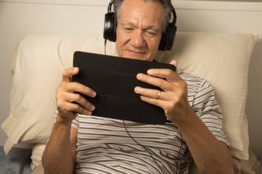 Kulaklık takmış, iPad 'inde film seyreden yetişkin bir adam.